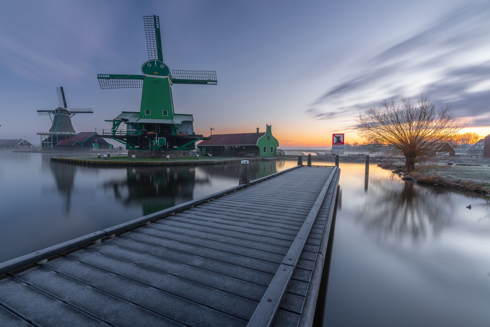 Windmills reflected in still water at blue hour, a jetty leading in