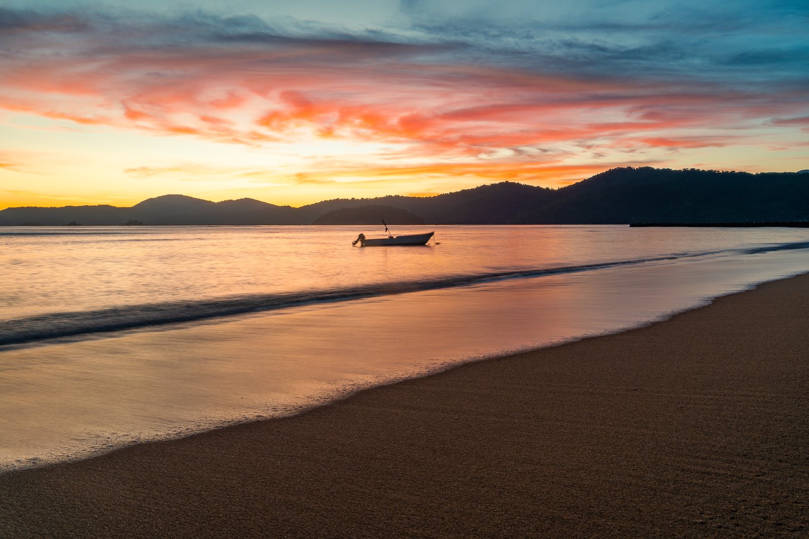 ゴールデンアワーの穏やかな水面に浮かぶ一艘のボート。低い太陽が空と濡れた砂を暖かなオレンジとピンクに染めている
