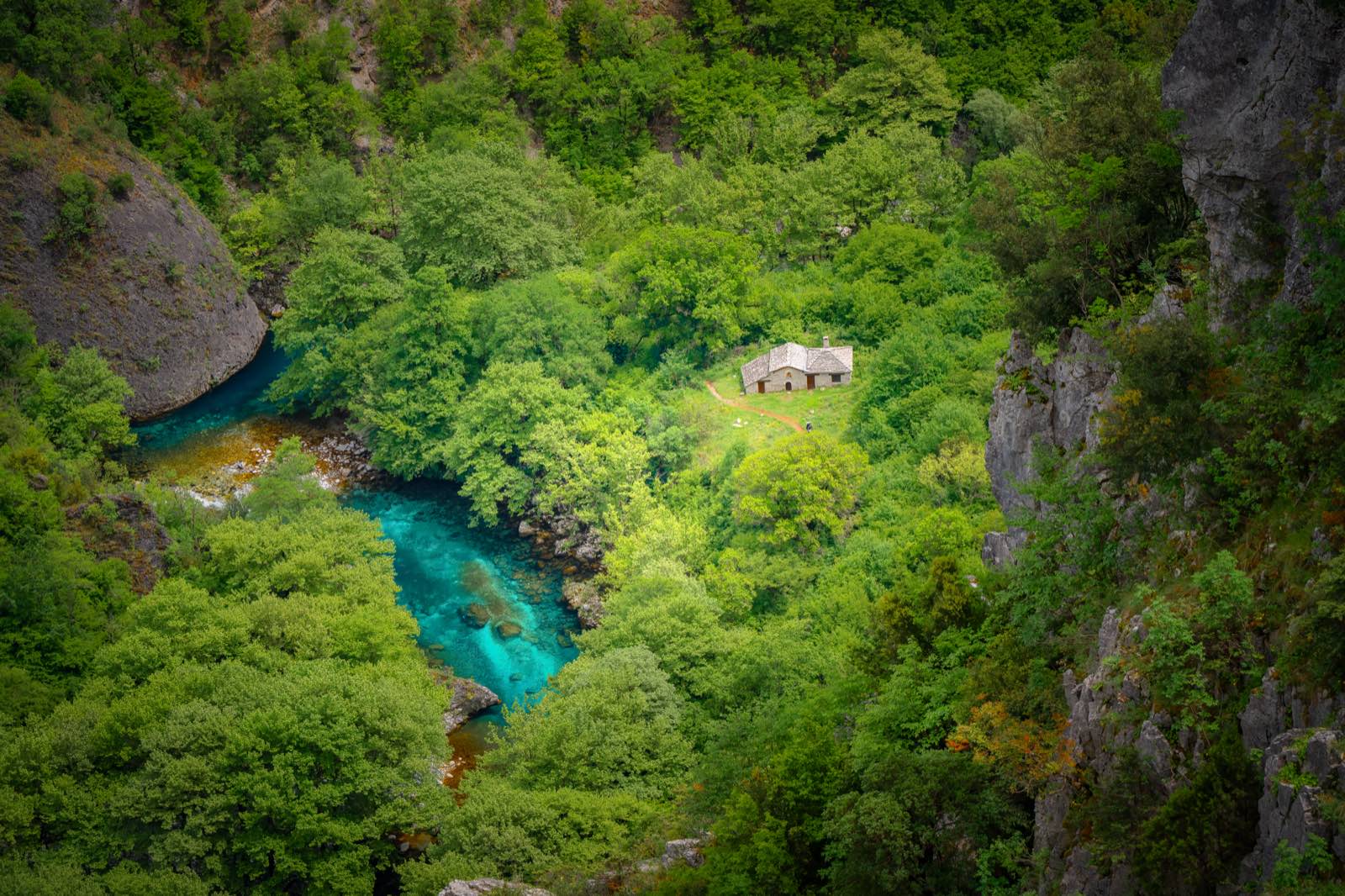 A tiny stone chapel on a green shelf deep in a limestone gorge, beside a river running vivid turquoise — a remote spot that clearly took scouting to find