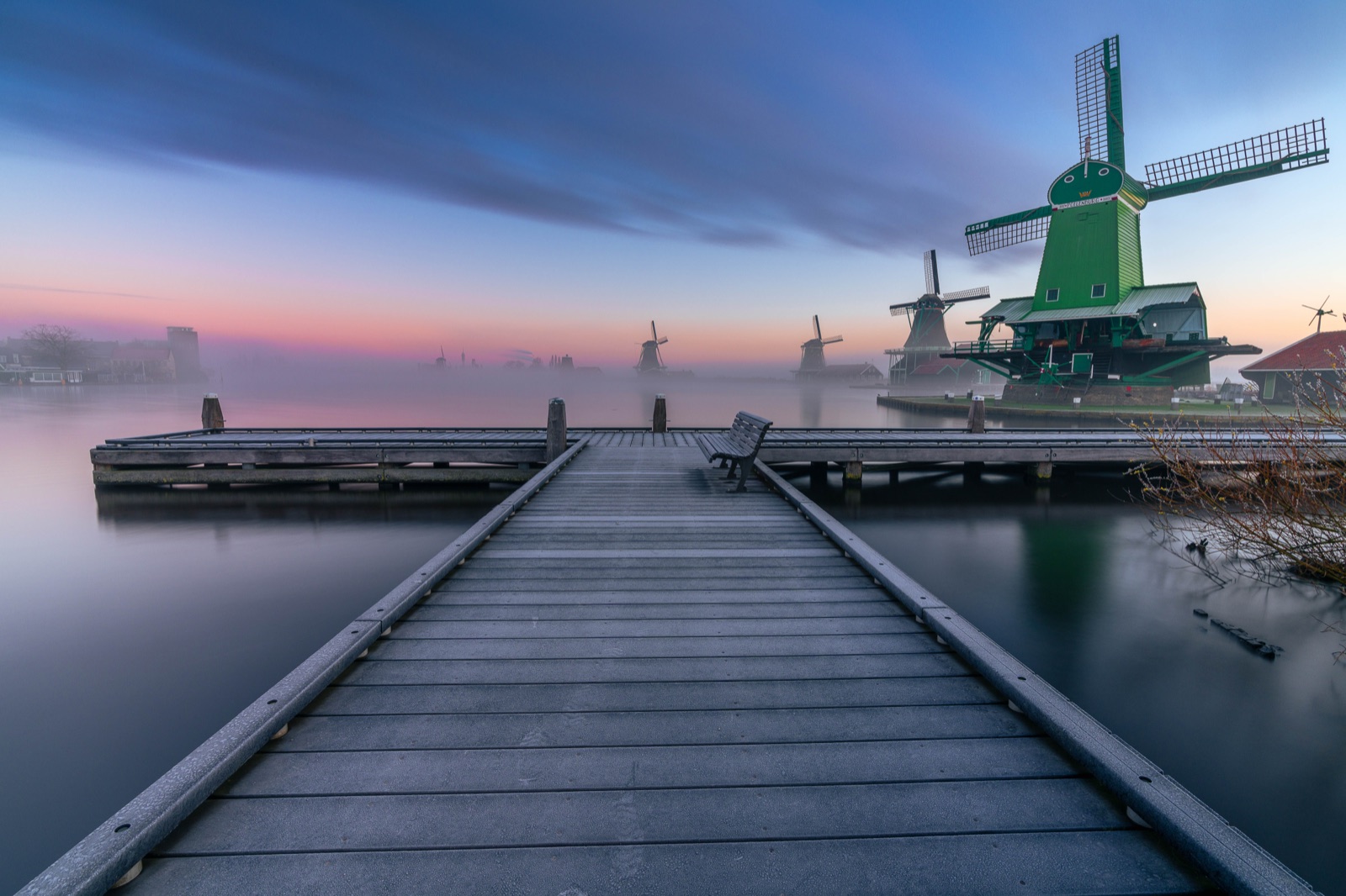 A long exposure of windmills with smooth water and a leading jetty
