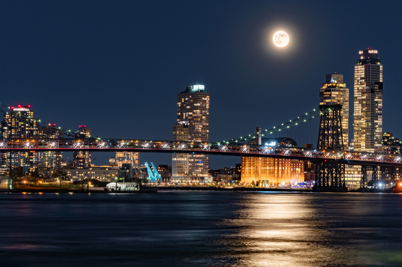 A full moon rising over a city skyline at blue hour