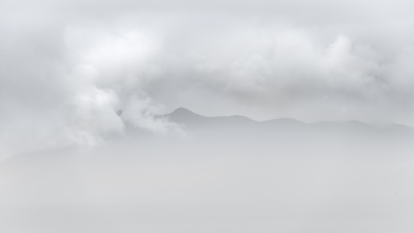 A mountain ridge and peak rising above a sea of cloud at dawn, soft high-key light