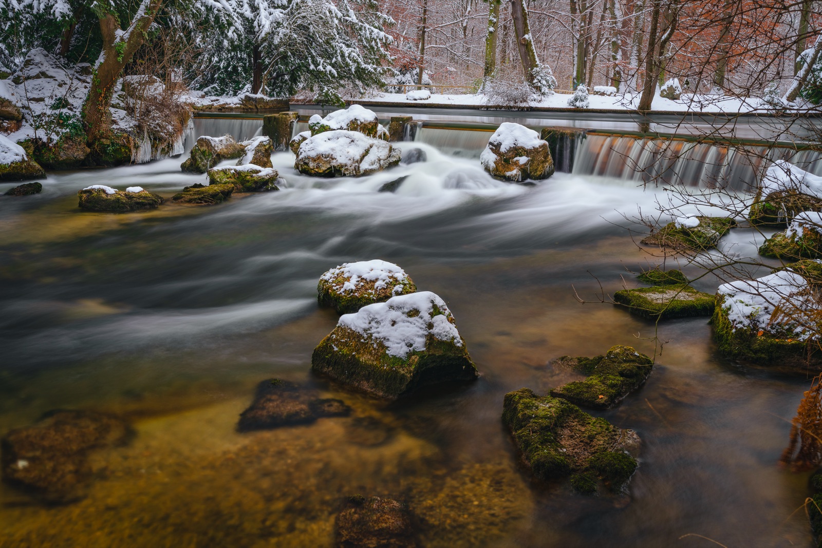 Eine schneebedeckte Landschaft bei tiefstehender Wintersonne, kahle Bäume werfen lange blaue Schatten über den makellos weißen Boden