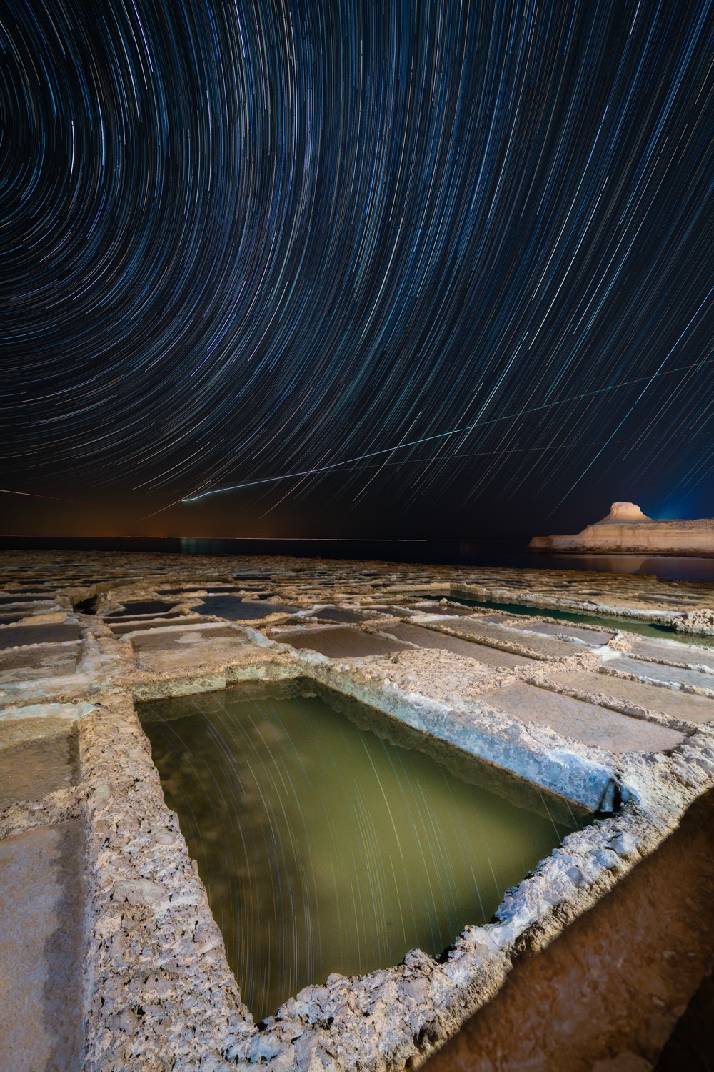 Concentric star trails wheeling over salt pools and a desert horizon
