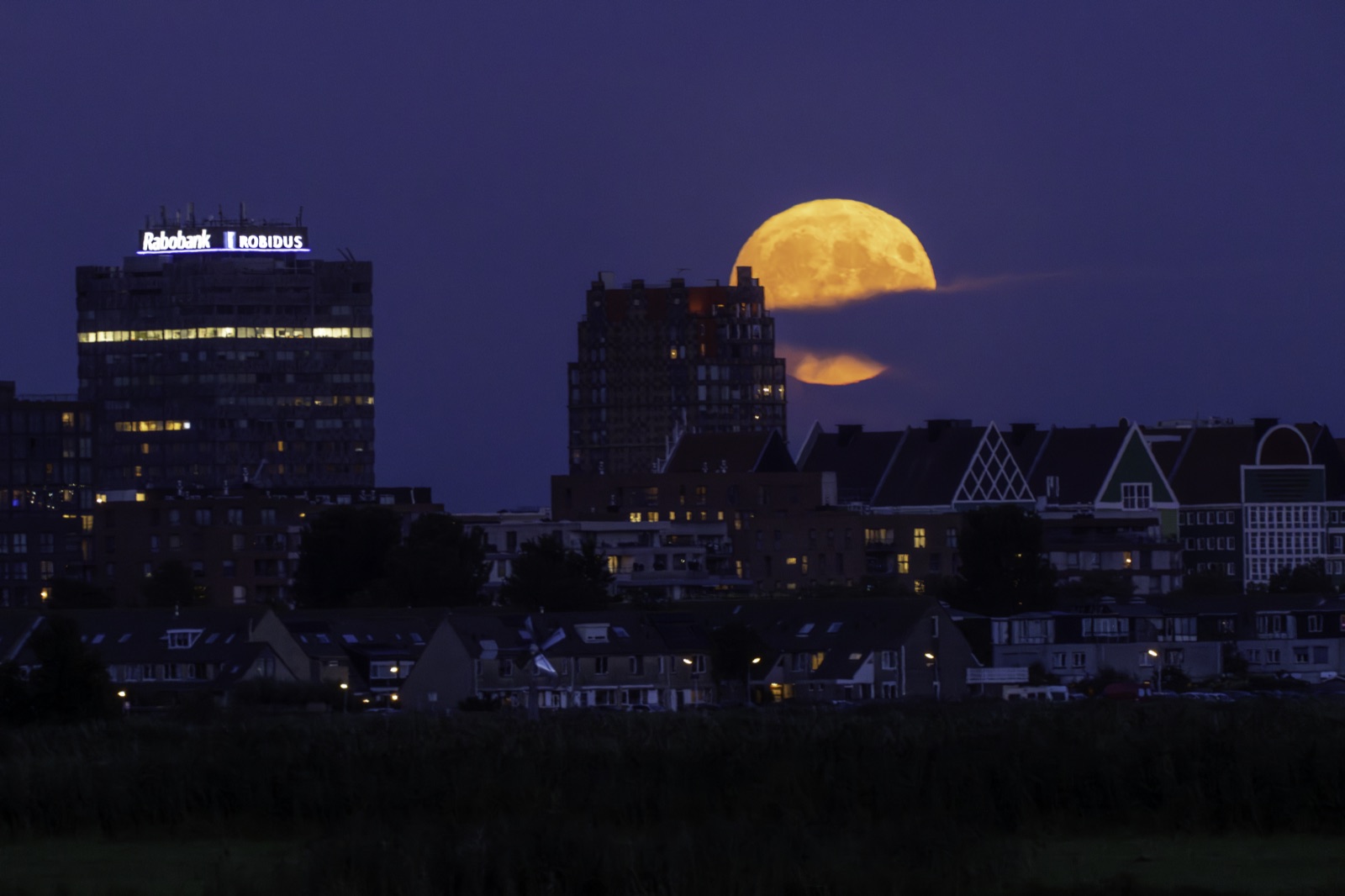 A large orange supermoon rising over a city skyline
